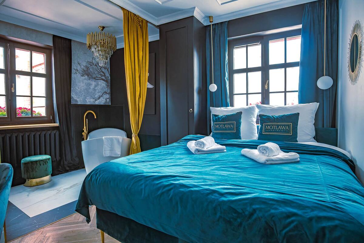 A hotel room with a large bed, a sitting area with a chair, a radiator, and a window with curtains.