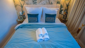 A neatly made bed with blue bedding and two pillows, a pair of rolled towels, and a wall with floral wallpaper. - Motlawa Apartments - Old Town by the river, Fast Wifi (Gdansk)