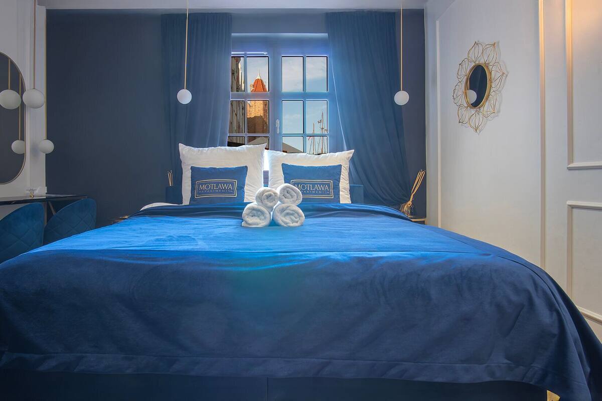 A hotel room with a large bed, a view of a cityscape through a window, and a decorative mirror on the wall.