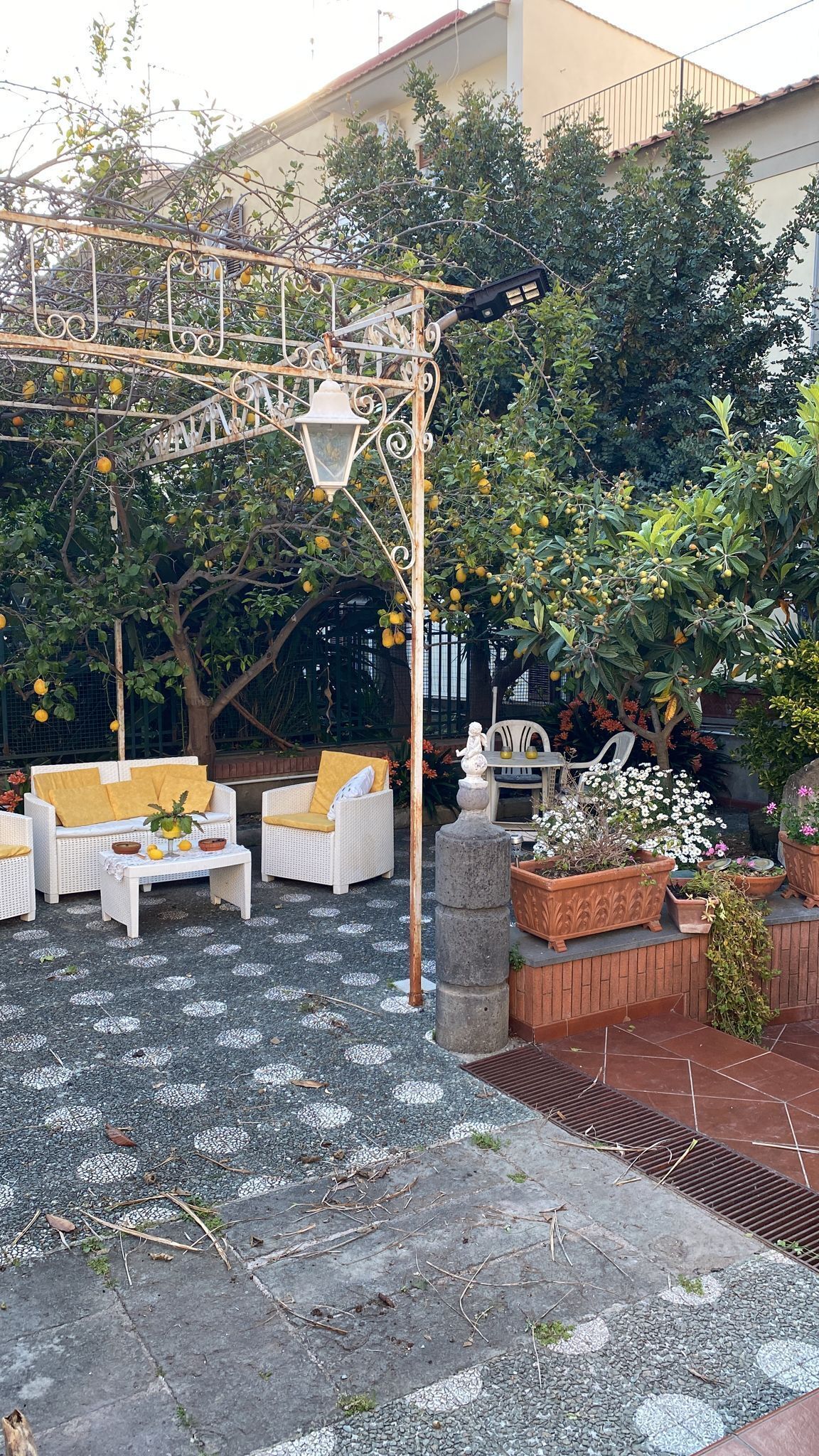 An outdoor seating area with wicker furniture, a pergola with a lantern, and potted plants.