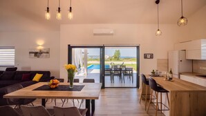 En moderne stue med spiseplads, et køkken og en skydedør til en pool.