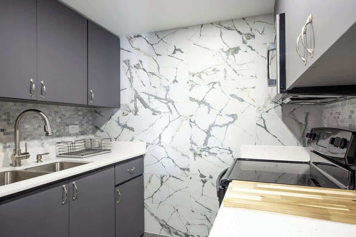 Una cocina moderna con armarios grises, salpicadero de mármol, electrodomésticos de acero inoxidable y encimera de madera.