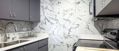 Una cocina moderna con armarios grises, salpicadero de mármol, electrodomésticos de acero inoxidable y encimera de madera.