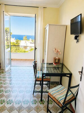 Ein Zimmer mit Balkon, Glastisch, Stühlen, Fernseher und Meerblick.
