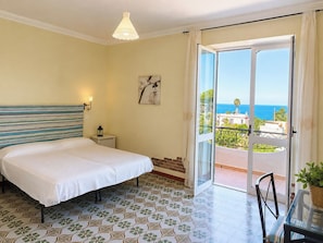 A hotel room with a bed, a nightstand, a lamp, a painting, a balcony with a view of the sea, and patterned floor tiles. - Panoramic studio apartment between the sea and the mountains - Forio d 'Ischia (Forio)