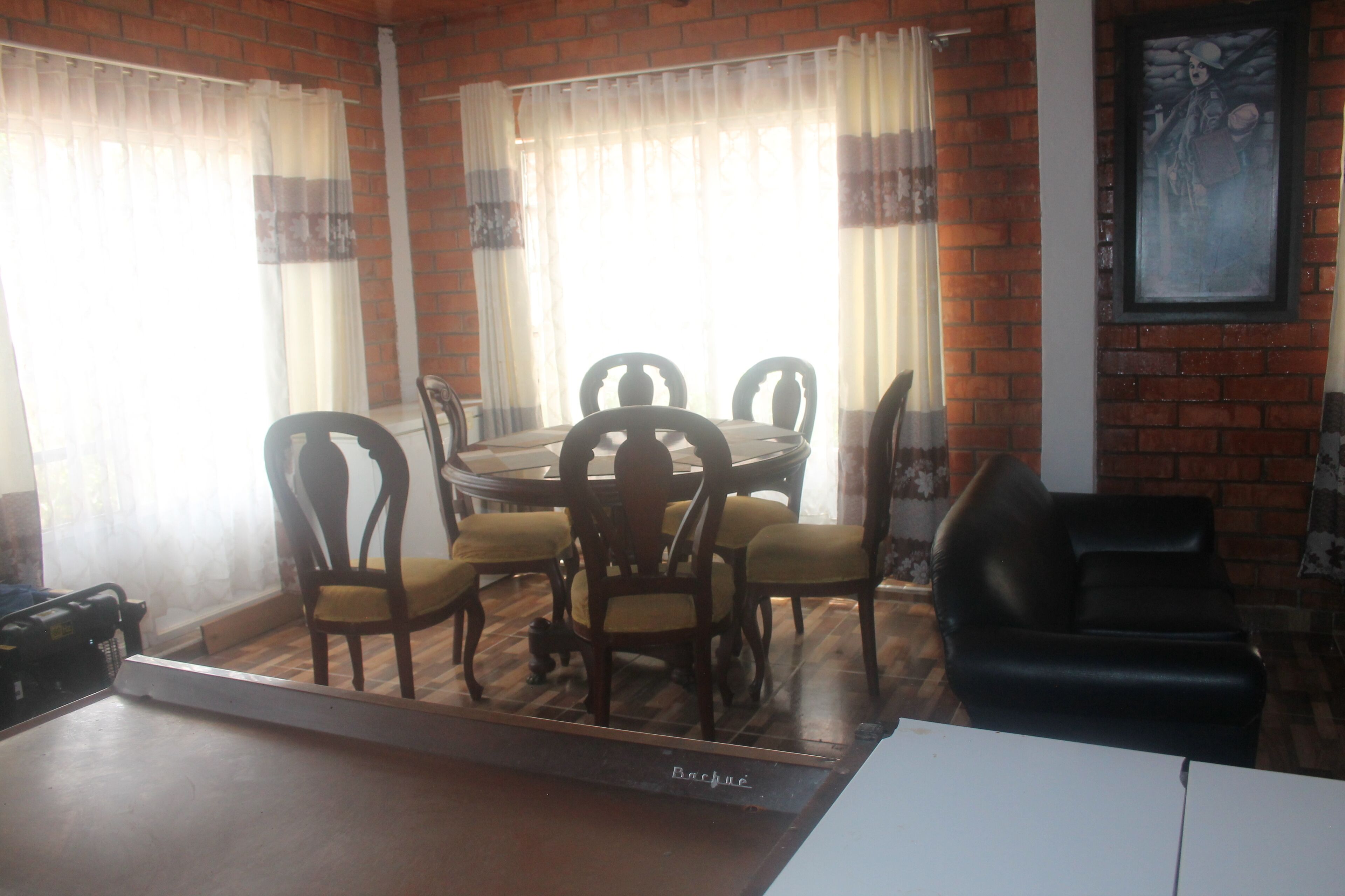 A dining area with a round table and chairs, a black leather sofa, and a brick wall with a framed picture.