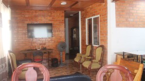 A room with brick walls, a flat-screen TV mounted on the wall, a fan, and several wooden chairs and tables. - Casa Campestre Para Descanso o Trabajo con Wifi, Cocina (carmen de apicala)