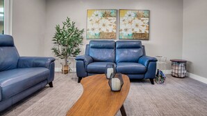 A living room with a blue leather sofa, a wooden coffee table, and two wall-mounted paintings.