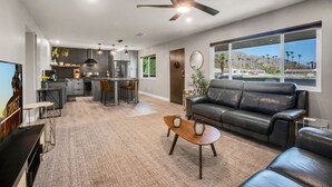 A modern living room with a leather sofa, a coffee table, and a dining area with a kitchen in the background.