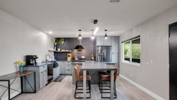 A modern kitchen with a central island, stainless steel appliances, pendant lighting, and a large window providing natural light.