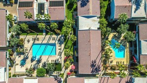 An aerial view of a residential area with multiple buildings, a swimming pool, and palm trees.