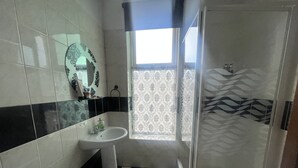 Une salle de bain avec un carrelage à motifs géométriques, un lavabo, un miroir et une douche.