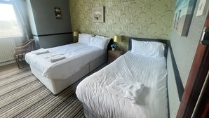 Une chambre d’hôtel avec deux lits, une chaise, une table de chevet et une fenêtre avec des rideaux.