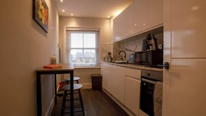 A compact kitchen with a window, a sink, a stove, and a small dining area with stools. - Beachside Family Flat, Central Weymouth (Weymouth)