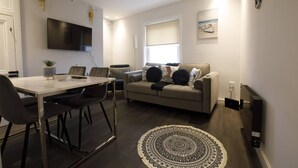 A modern living room with a dining area, a sofa, and a TV mounted on the wall. - Beachside Family Flat, Central Weymouth (Weymouth)