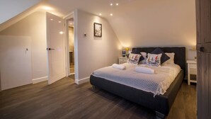 A bedroom with a sloped ceiling, a bed with sailboat-themed pillows, a bedside table with a lamp, and a door leading to another room. - Beachside Family Flat, Central Weymouth (Weymouth)