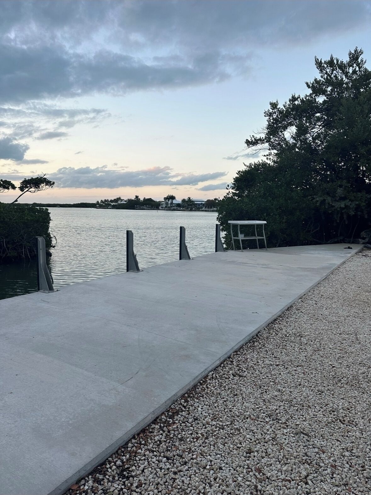 A concrete dock extending into calm water, surrounded by trees and a clear sky.