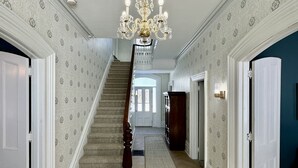 A spacious hallway with a herringbone-patterned wooden floor, a grand staircase, and a chandelier. - Stunning Century Riverfront Estate with sweeping waterfront views. (Napanee)