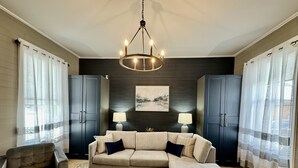 A living room with a beige sofa, two lamps, a chandelier, and dark wooden cabinets. - Stunning Century Riverfront Estate with sweeping waterfront views. (Napanee)