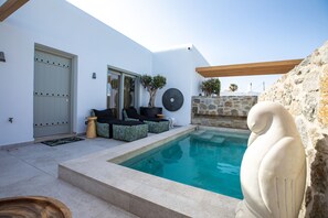 A modern outdoor pool area with a stone wall, a statue, and outdoor seating. - Deluxe Zirkon Suite with Private Pool (Mykonos)