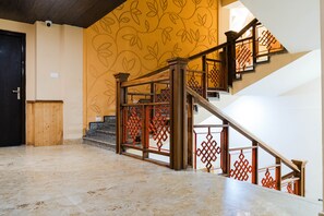 A spacious room with a marble floor, a wooden door, and a staircase with red lattice railings. - Bliss Hungry Jack (Gangtok)