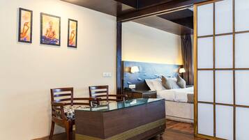 A room with a wooden desk, two chairs, a bed with a blue headboard, and three framed pictures on the wall.