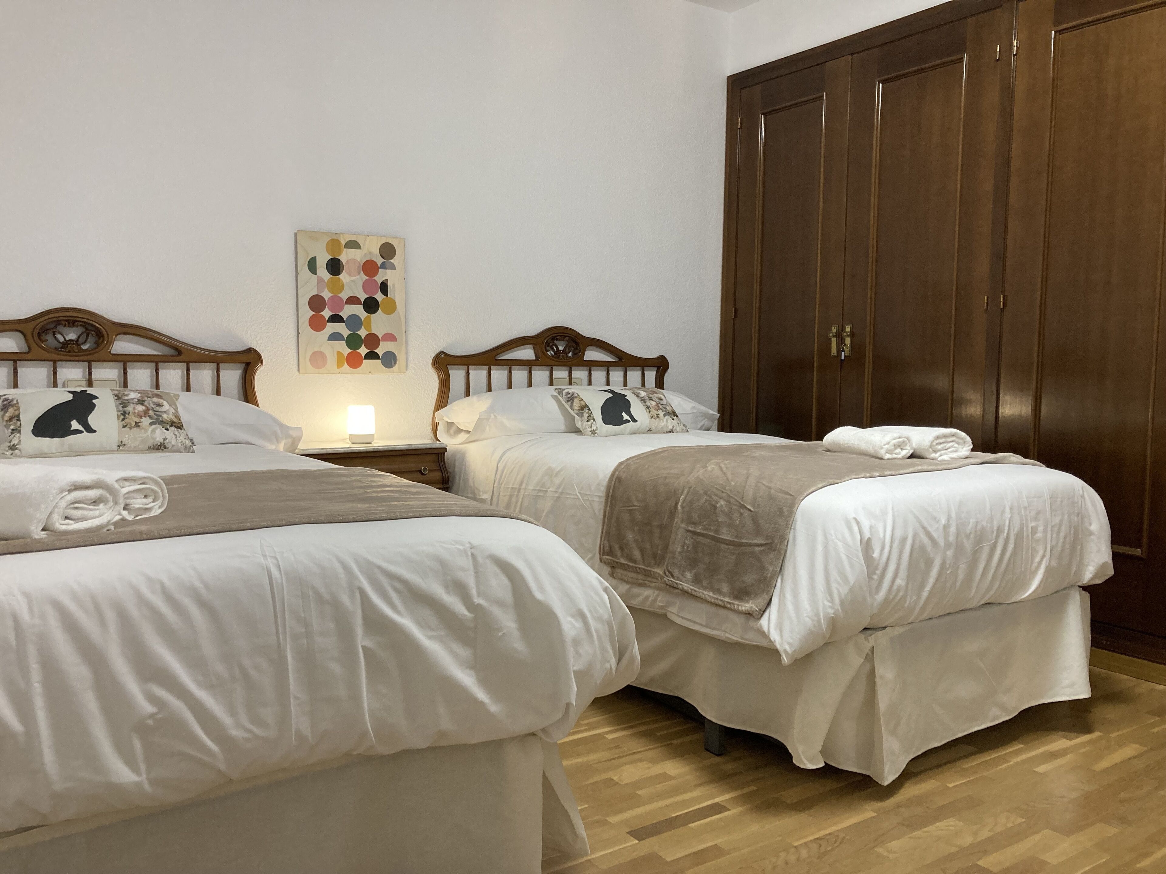 Una habitación de hotel con dos camas, un armario de madera y una obra de arte en la pared.