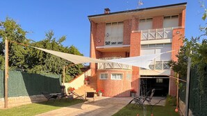 Un patio trasero residencial con una casa de ladrillo de dos pisos, un dosel blanco, un módulo de juegos amarillo y una planta en maceta.