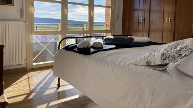 Un dormitorio con una cama grande, un armario de madera y vistas al campo a través de un ventanal corredera.