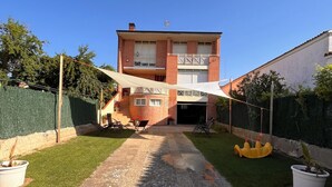 Un edificio de dos pisos con garaje, un patio cubierto y un camino de entrada pavimentado.