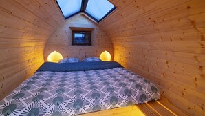A cozy, sloped-roofed room with a bed, a skylight, and a small window.