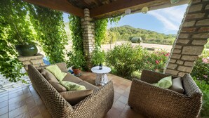 A covered patio area with wicker furniture, a stone pillar, and a view of a green landscape.