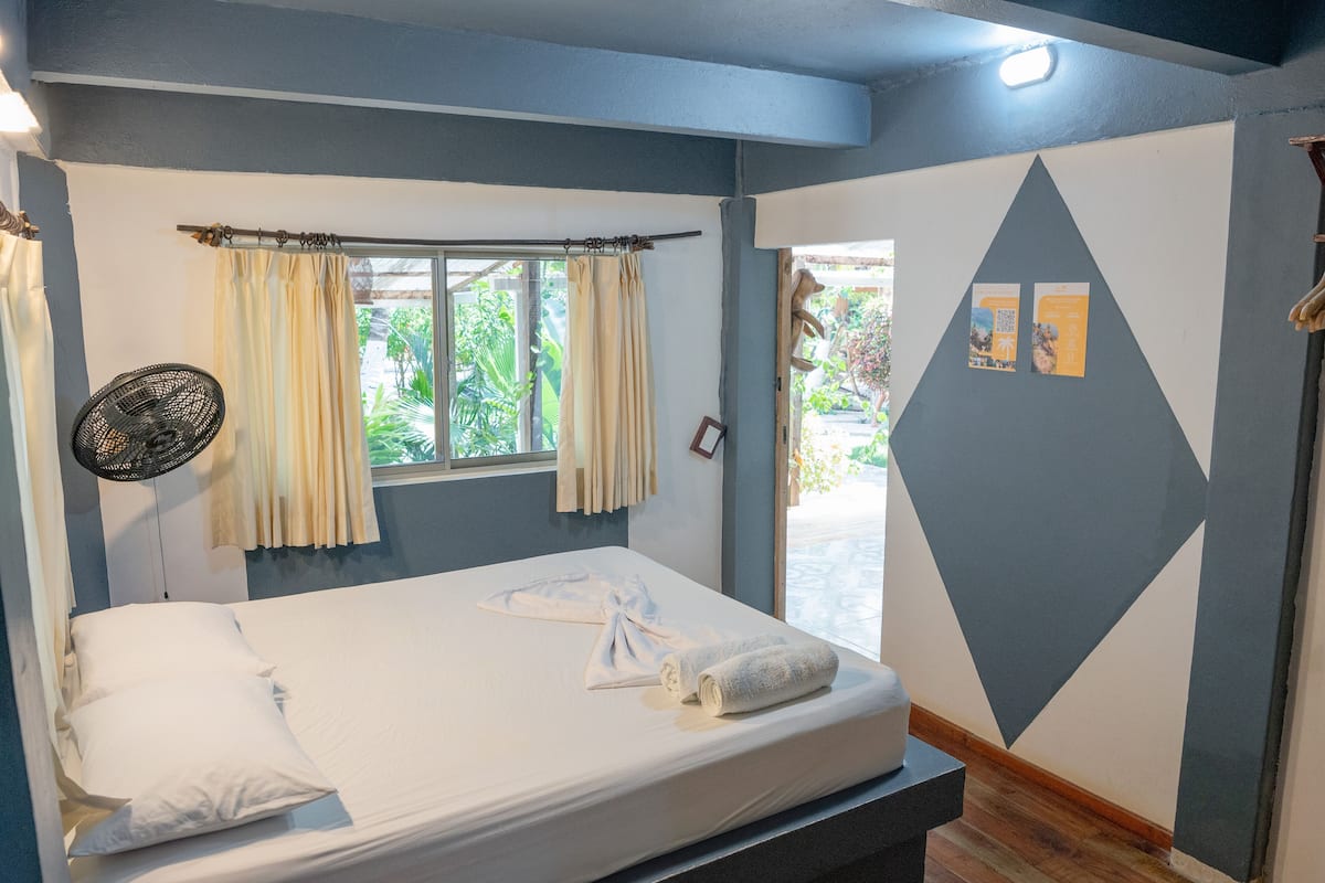 Una cama bien hecha con sábanas blancas, una ventana con cortinas y una pared con un diseño geométrico.