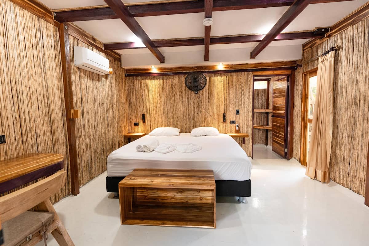 Un dormitorio con un panel de madera en la pared, una cama con ropa de cama blanca, una mesita de noche y un banco de madera.