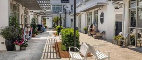 A pedestrian street with white buildings, outdoor seating, and potted plants.