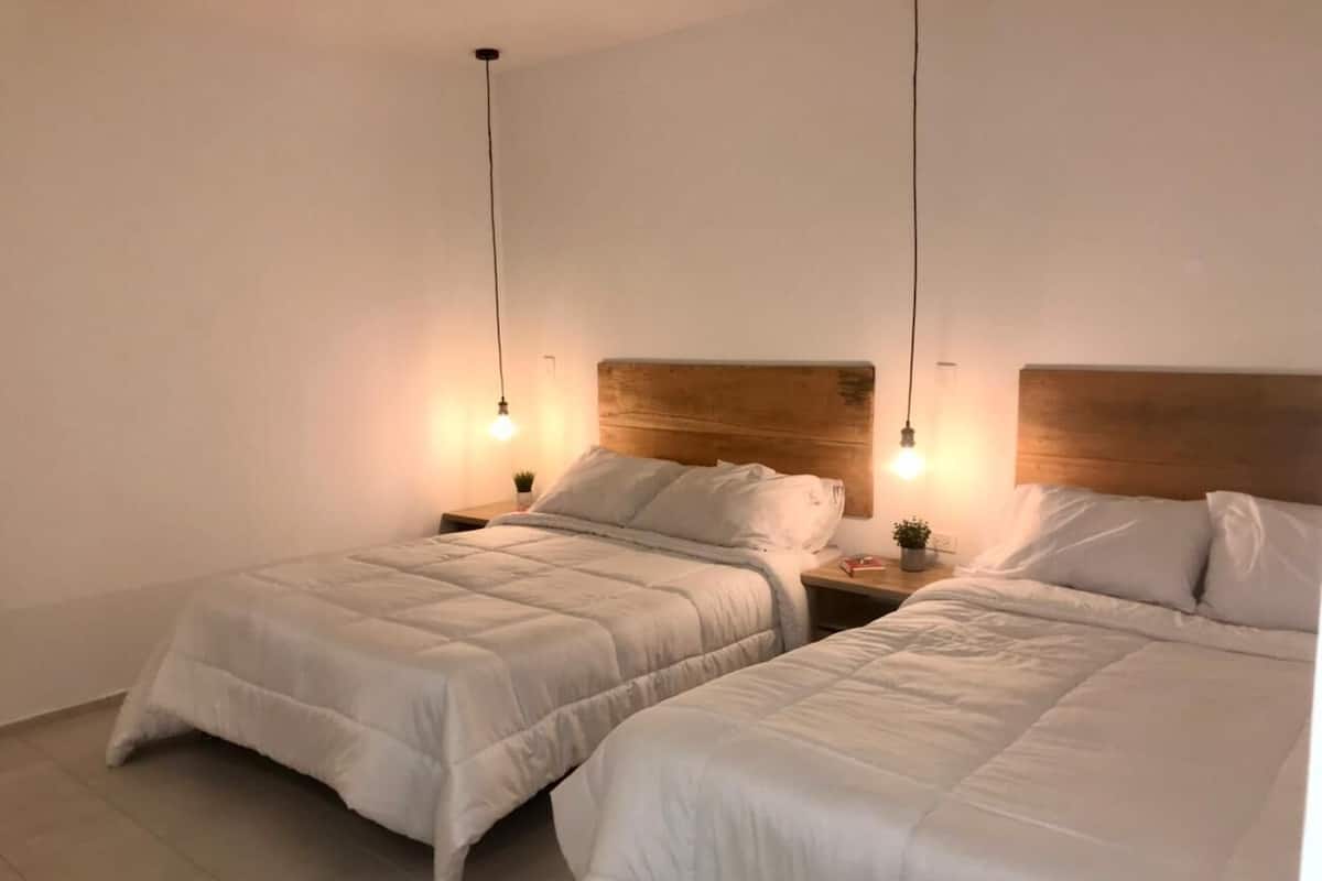 A bedroom with two beds, each with a wooden headboard, bedside tables, and wall-mounted lamps.