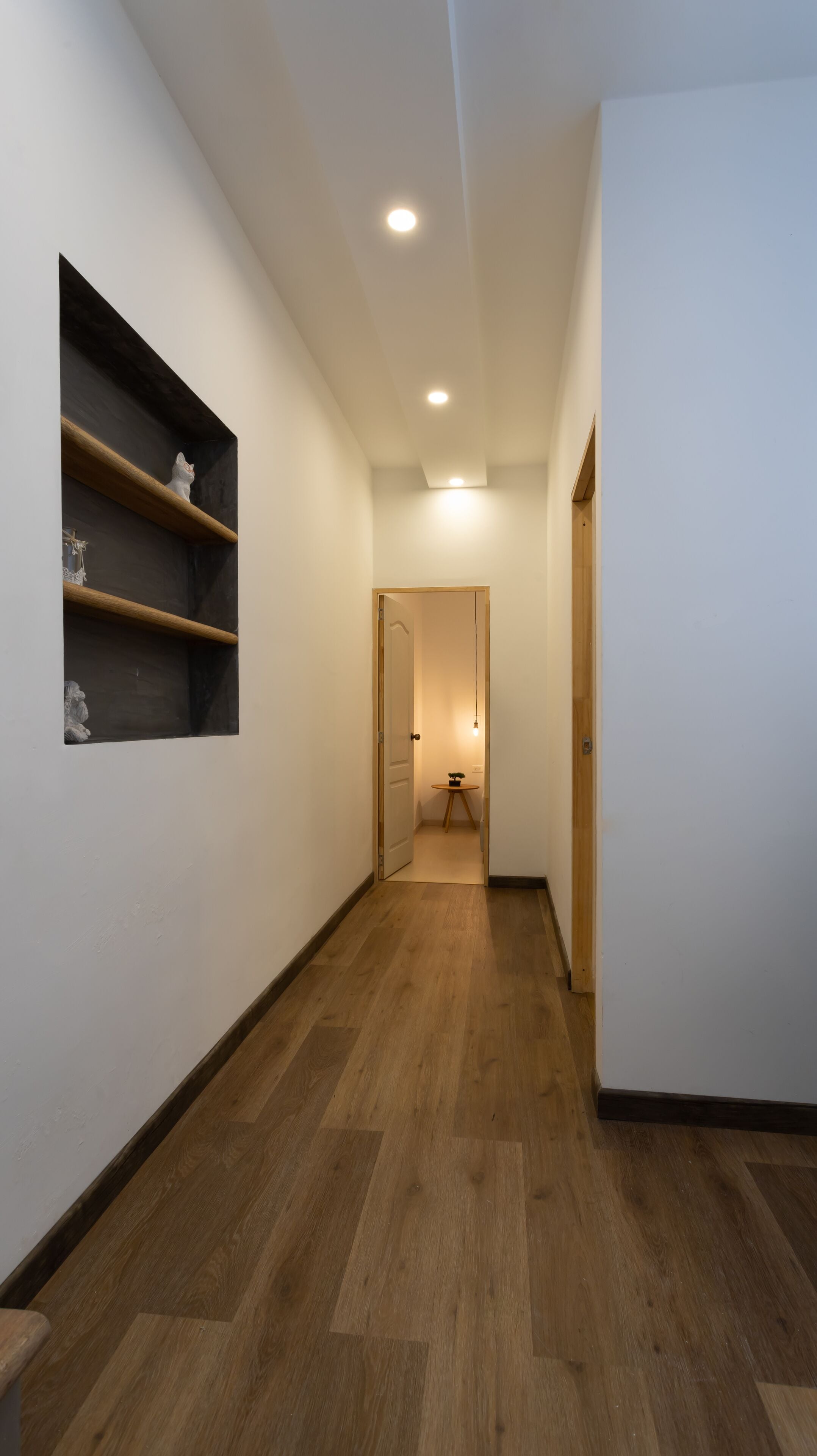 Un couloir doté d’un plancher en bois, de murs blancs et d’une porte au fond.
