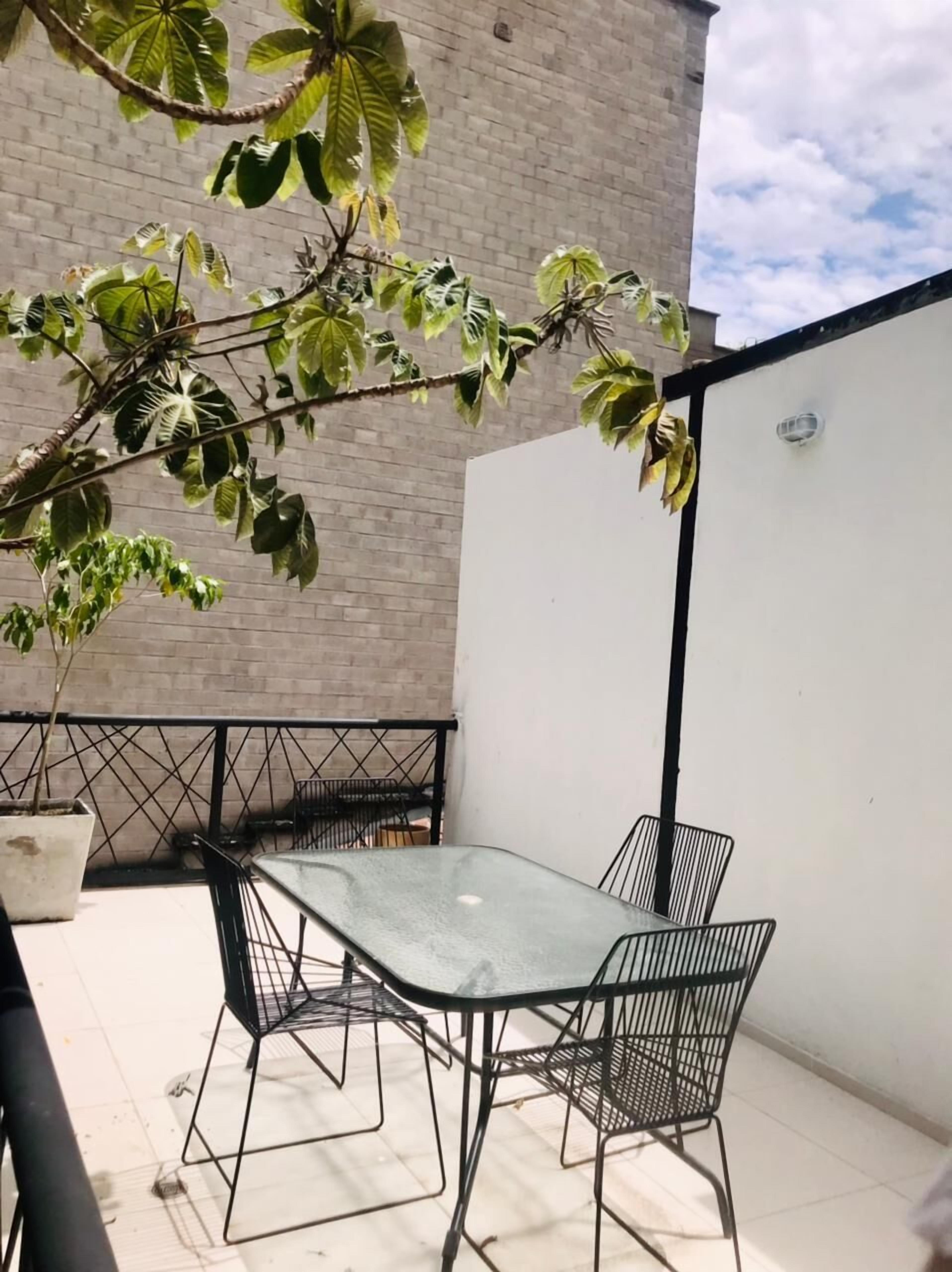 An outdoor patio with a glass table and metal chairs, surrounded by a brick wall and a white fence.