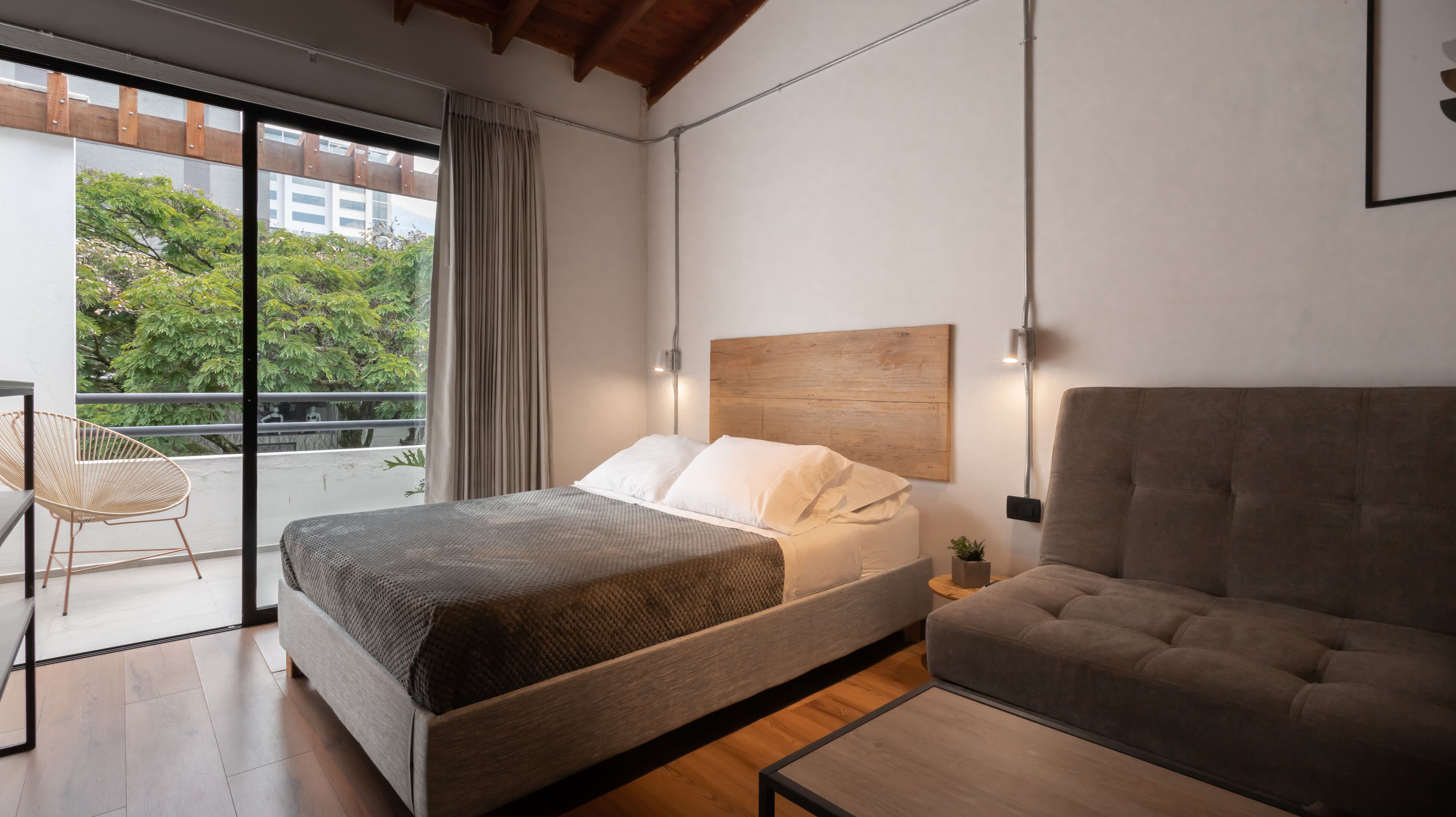 Un dormitorio moderno con cama, sofá, sillón y vistas al exterior.