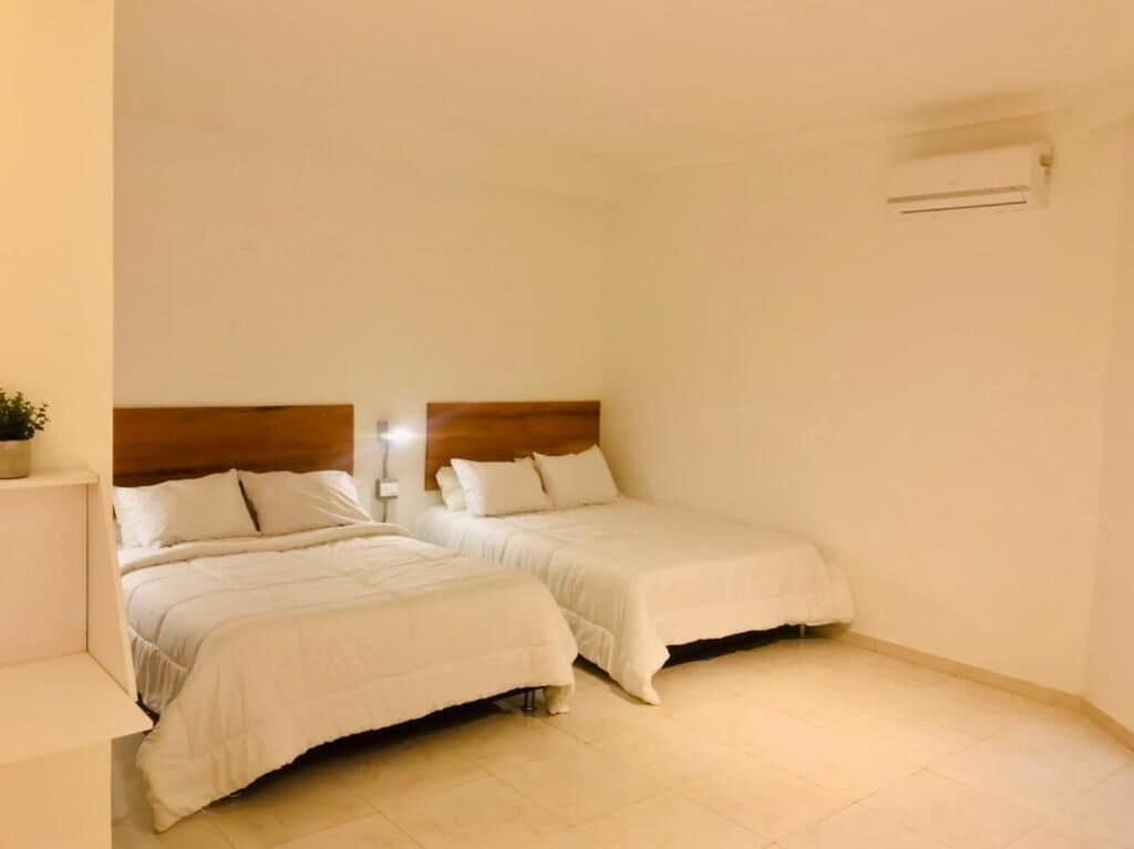 A room with two beds, a wooden headboard, a nightstand, and an air conditioning unit.