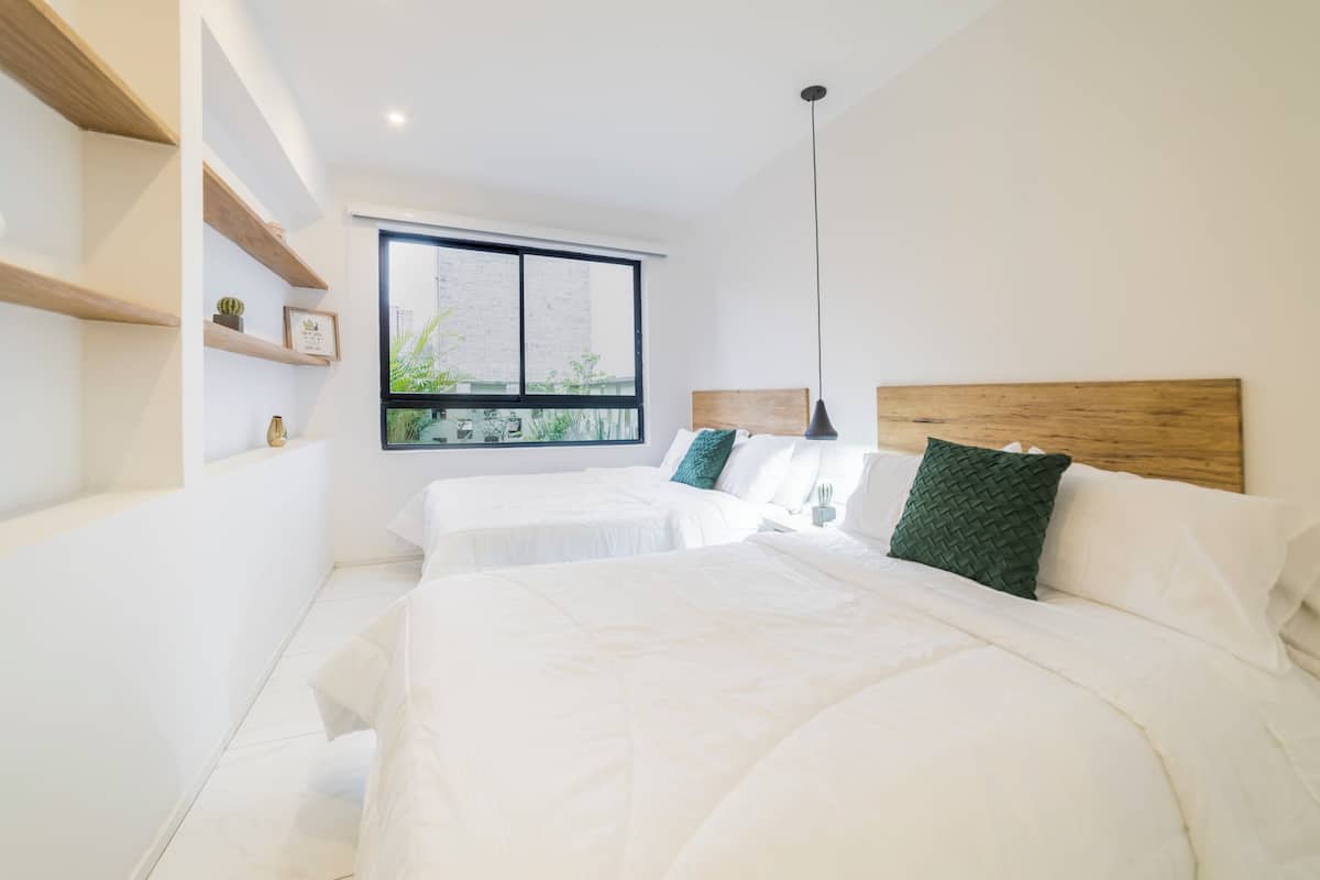 A modern bedroom with two beds, a large window, and built-in shelves.