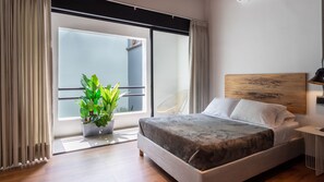 A modern bedroom with a large bed, a potted plant, and a view of the outside through a sliding glass door. - Soy Local Primavera  (Medellín)