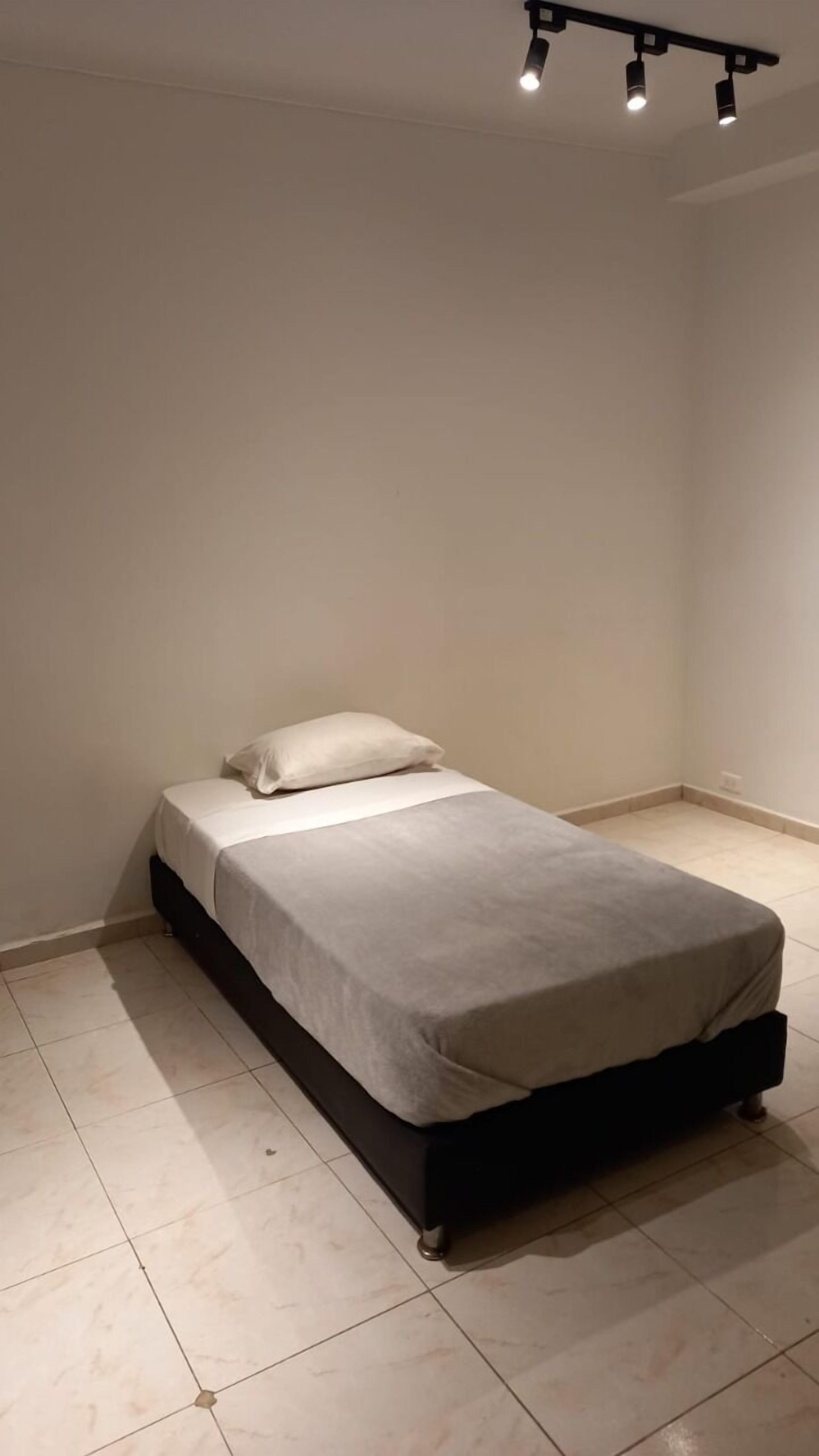 Ein Einzelbett in einem Zimmer mit einer schlichten weißen Wand und einem gefliesten Boden.