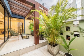 A modern outdoor patio with a glass door entrance, wooden beams, and potted plants. - Soy Local Primavera  (Medellín)