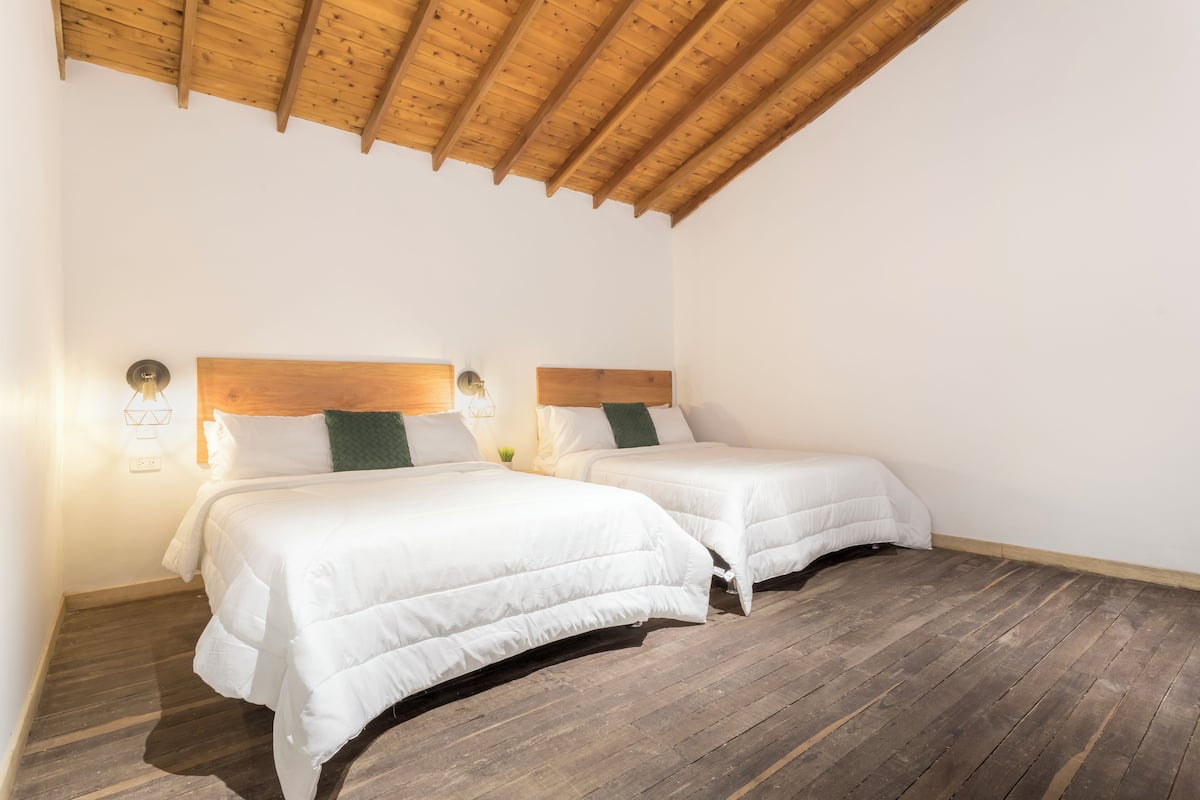 A room with two beds, wooden ceiling beams, and a wooden floor.