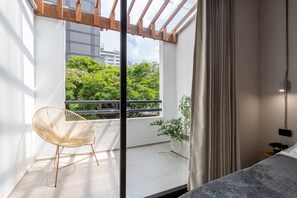 A modern bedroom with a large window, a wicker chair, a potted plant, and a bed. - Soy Local Primavera  (Medellín)