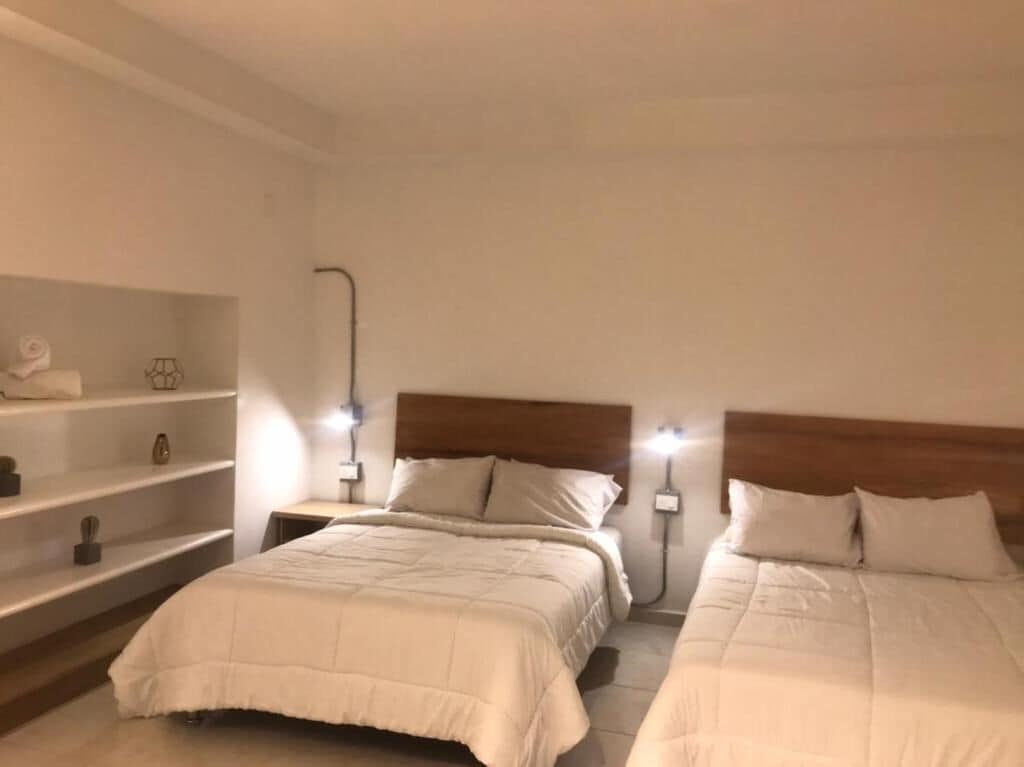 Ein Hotelzimmer mit zwei Betten, einer Ablage für Toilettenartikel und Nachttischlampen.