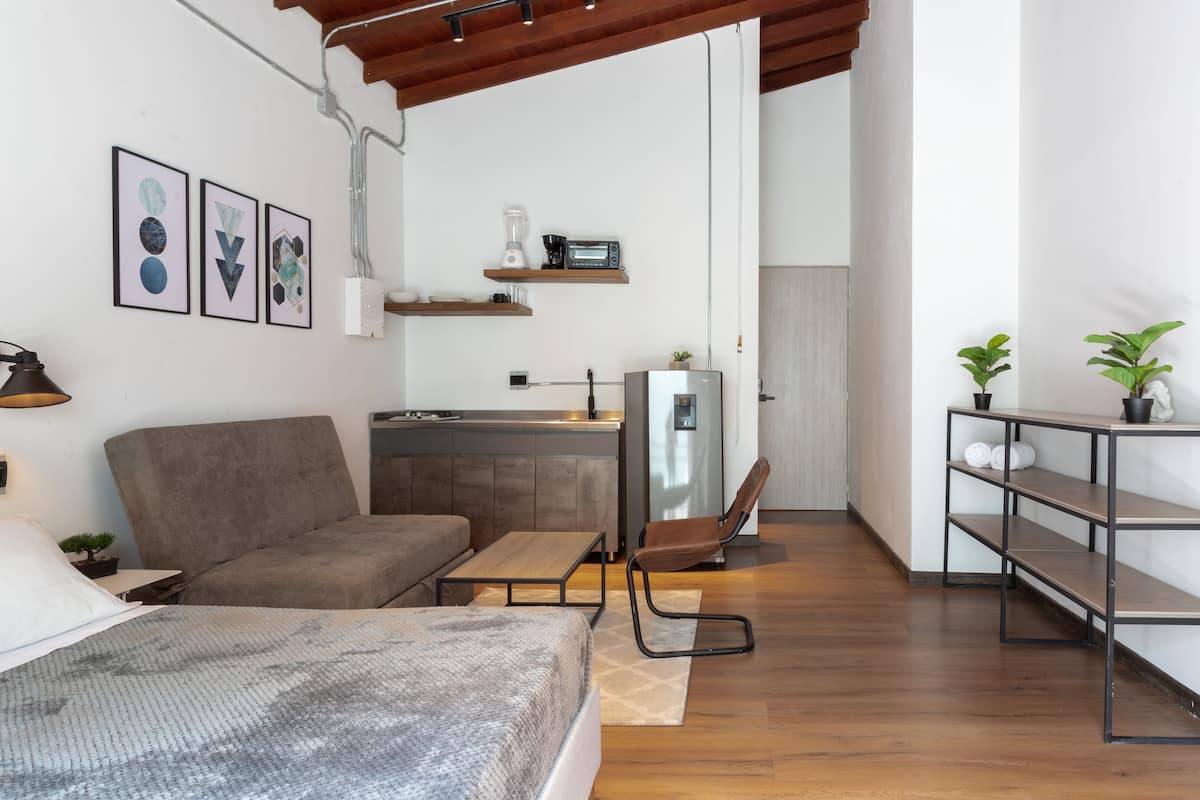 A compact living space with a sofa, a dining table, a kitchenette, and a TV mounted on the wall.