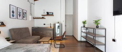 A compact living space with a sofa, a dining table, a kitchenette, and a TV mounted on the wall.