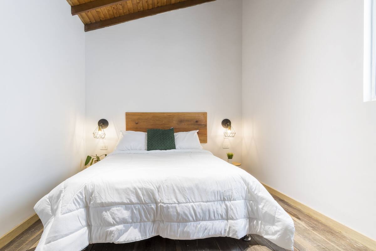 A neatly made bed with white bedding, a wooden headboard, and two bedside lamps.
